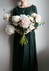 An elegant faceless woman in a green dress holding a big bouquet of white and pastel peonies, cottagecore and green academia aesthetic