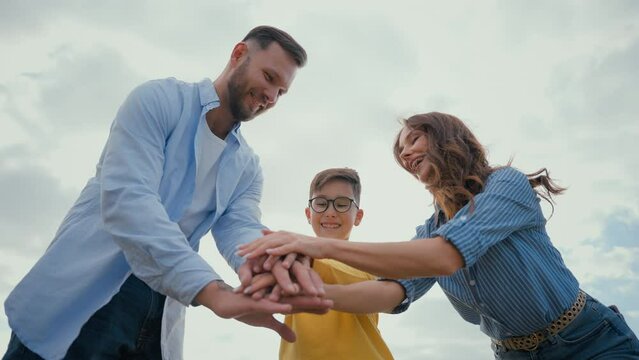 Caucasian happy family woman female mom male man dad putting stack hand little boy son child kid hands holding together raise arms air sky showing unity successful team gesture winner teamwork victory