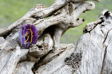 A close up image of an deep purple amethyst crystal with a healing spiritual symbol written on it. 