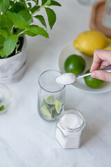 Homemade mojito cocktail drink preparing process, person placing sugar in glass with mint and lime, ingredients for mojito recipe.