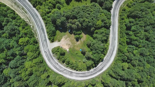 Aerial view of winding asphalt mountain road among green trees in summer.