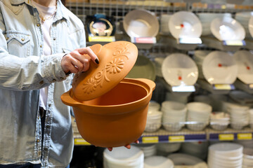 A woman is holding a clay pan or pot with a lid in a store