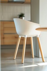 White plastic dining chair & beechwood side table on concrete floor, light wooden cabinets backdrop, closeup, soft shadows.