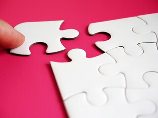 A close-up of a hand finishing or completing a white jigsaw puzzle by placing the last piece...