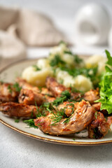 Baked or fried chicken necks in barbecue sauce, cauliflower and lettuce leaves on a plate on the table. A healthy dinner on a light gray background in closeup. Proper nutrition