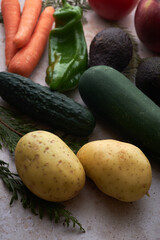 A variety of fresh vegetables including green bell pepper, cucumbers, carrots, potatoes, and avocados on a light surface.