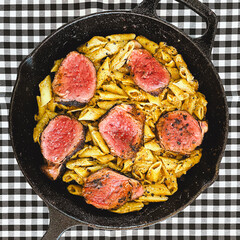 Penne Pasta with Roast Beef Slices in a Cast Iron Skillet on a Rustic Checkered Tablecloth