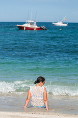Fototapeta premium Mature Mexican woman sitting on a beach enjoying summer vacations in Los Barriles Baja California Sur Mexico, with blue sea and waves, fishing boats in the background. Amazing Sea of Cortes