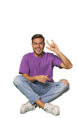 Casual man sitting on floor showing a horns gesture as a revolution concept.