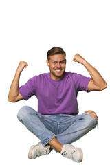 Casual man sitting on floor showing strength gesture with arms, symbol of feminine power