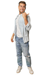 Fototapeta premium Full body portrait of a man in studio points with thumb finger away, laughing and carefree.