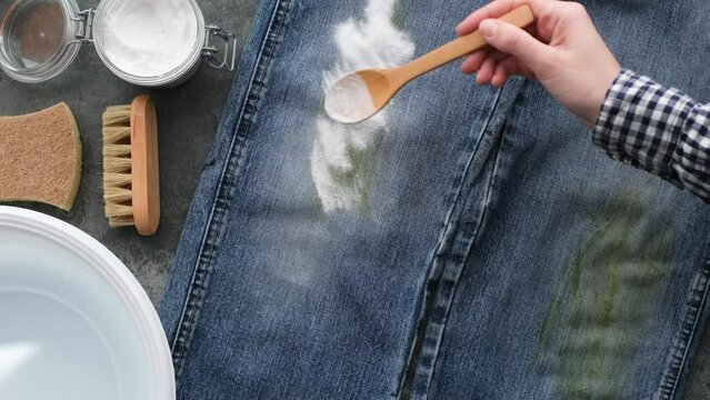 Dirty stains of fresh green grass on jeans. Woman's hand applies baking soda powder for eco-friendly stain removal. Zero waste concept. top view. 4k video