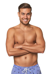 Fototapeta premium Shirtless young man in swimsuit against a studio backdrop, embodying summer vibes