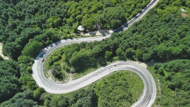 Aerial view of winding asphalt mountain road among green trees in summer.