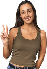 Hispanic young woman showing victory sign and smiling broadly.