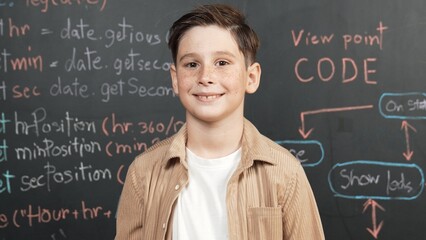 Panorama shot of happy caucasian boy smiling and standing at blackboard with engineering code or...