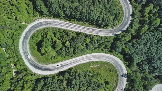 Aerial view of winding asphalt mountain road among green trees in summer.