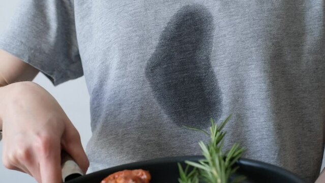 Splashing grease stain on gray clothes. An unrecognizable woman a frying pan with meat and herbs. daily life stain concept. 4k video