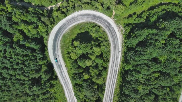 Aerial view of winding asphalt mountain road among green trees in summer.