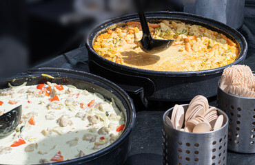 Thai curry in large pots at street food stall, creamy sauce, vegetable chunks, red peppers, food festival