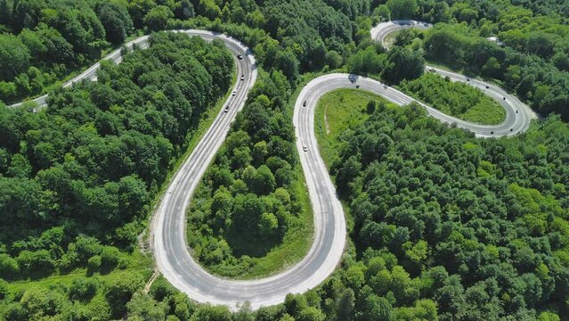 Aerial view of winding asphalt mountain road among green trees in summer.