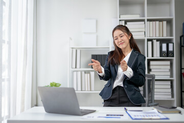 Confident businesswoman in a modern office, smiling and gesturing at laptop while working remotely. Professional workplace setup.