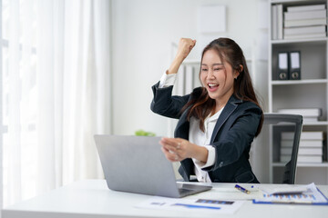 Excited businesswoman celebrating a success at work, raising her fist in victory while working on a...