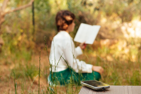 the girl is reading a book in the background, the phone is in the foreground, day of silence, dopamine detox,  horizontal photo