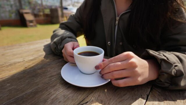 Close-Up of Female Hands Holding a Coffee Cup on a Wooden Table in a Rural Environment. Woman Holding Coffee Cup in Rustic Outdoor Setting