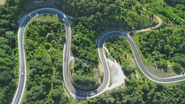 Aerial view of winding asphalt mountain road among green trees in summer.
