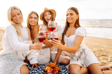 Hen party on the beach. Young ladies with glasses of wine embracing posing standing on the beach. Vacation, relax.
