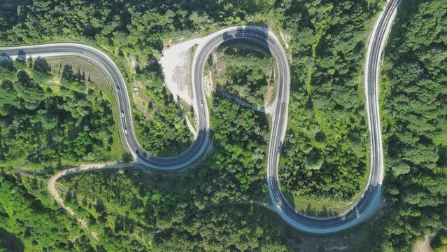 Aerial view of winding asphalt mountain road among green trees in summer.