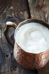 Turkish ayran in a traditional copper mug on an old wooden table, close-up of the drink top view