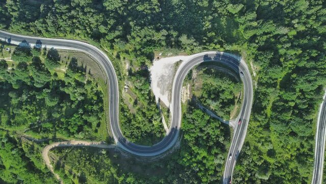 Aerial view of winding asphalt mountain road among green trees in summer.