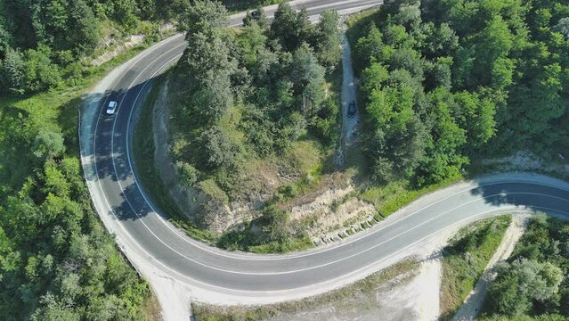 Aerial view of winding asphalt mountain road among green trees in summer.