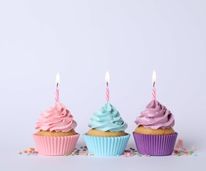 Delicious birthday cupcakes with burning candles and sprinkles on light grey background