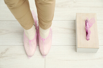 Woman wearing pink shoe covers onto her boots indoors, top view