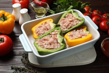 Raw stuffed peppers in dish and ingredients on wooden table