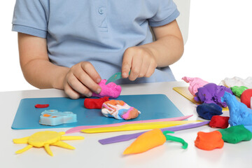 Little boy sculpting with play dough at table on white background, closeup