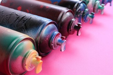 Many spray paint cans on pink background, closeup