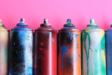 Many spray paint cans on pink background, flat lay