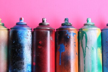 Many spray paint cans on pink background, flat lay