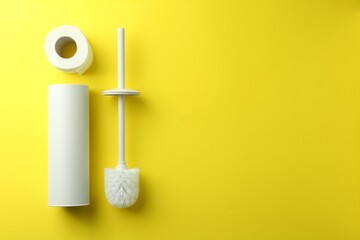 Toilet brush, holder and roll of paper on yellow background, flat lay. Space for text