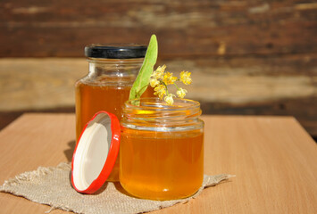 fresh honey in a glass jar with a linden flower on the table. blurred background