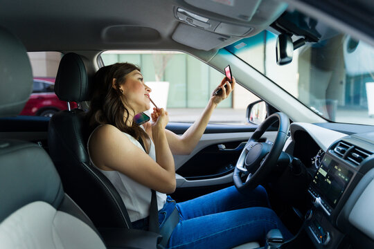 Concentrated woman applies lipstick and holds a phone, highlighting the dangers of multitasking behind the wheel