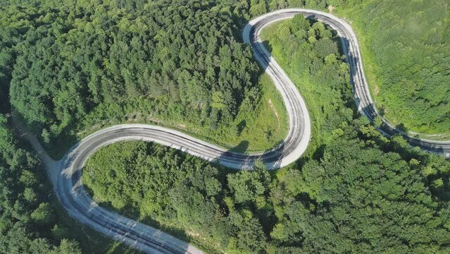 Aerial view of winding asphalt mountain road among green trees in summer.