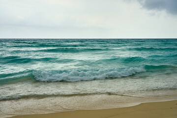 Waves and foam on a tropical sandy beach with clouds.