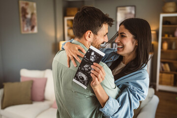 Happy pregnant woman with her husband watch ultrasound photo of baby