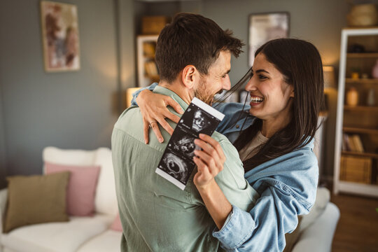 Happy pregnant woman with her husband watch ultrasound photo of baby