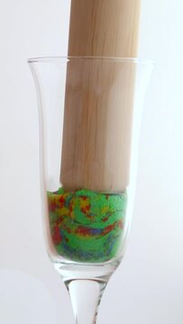 The colorful kinetic sand of the cubes is crushed in a glass. Multicolored geometric figures made of kinetic sand are crushed in a glass mug.